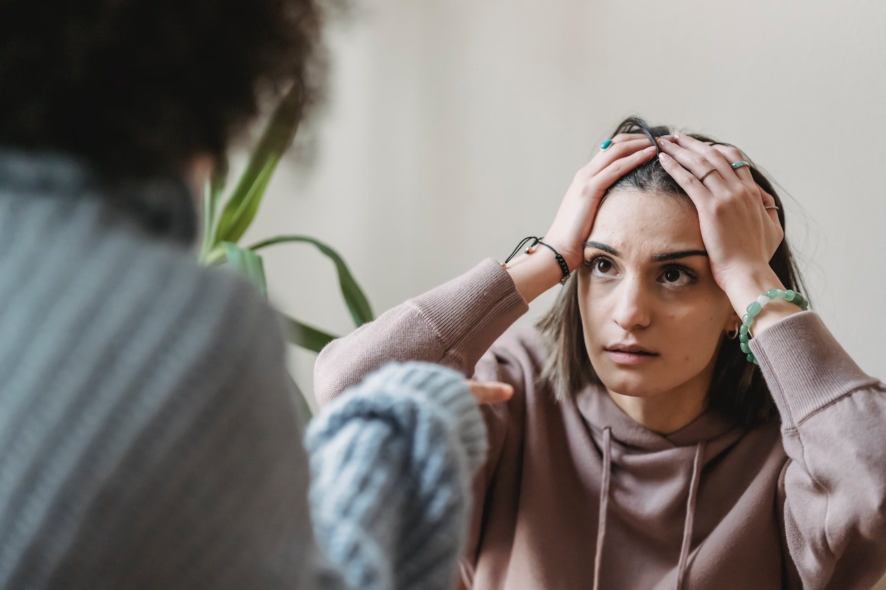 Woman is holding her head and arguing with other woman.