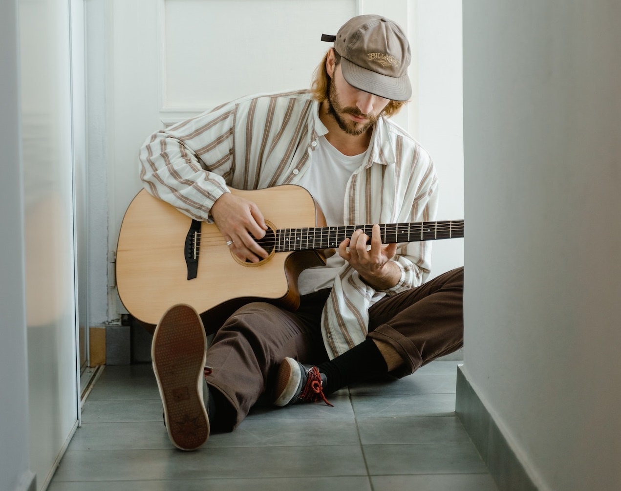 Man is seating on the floor and playing a guitar.