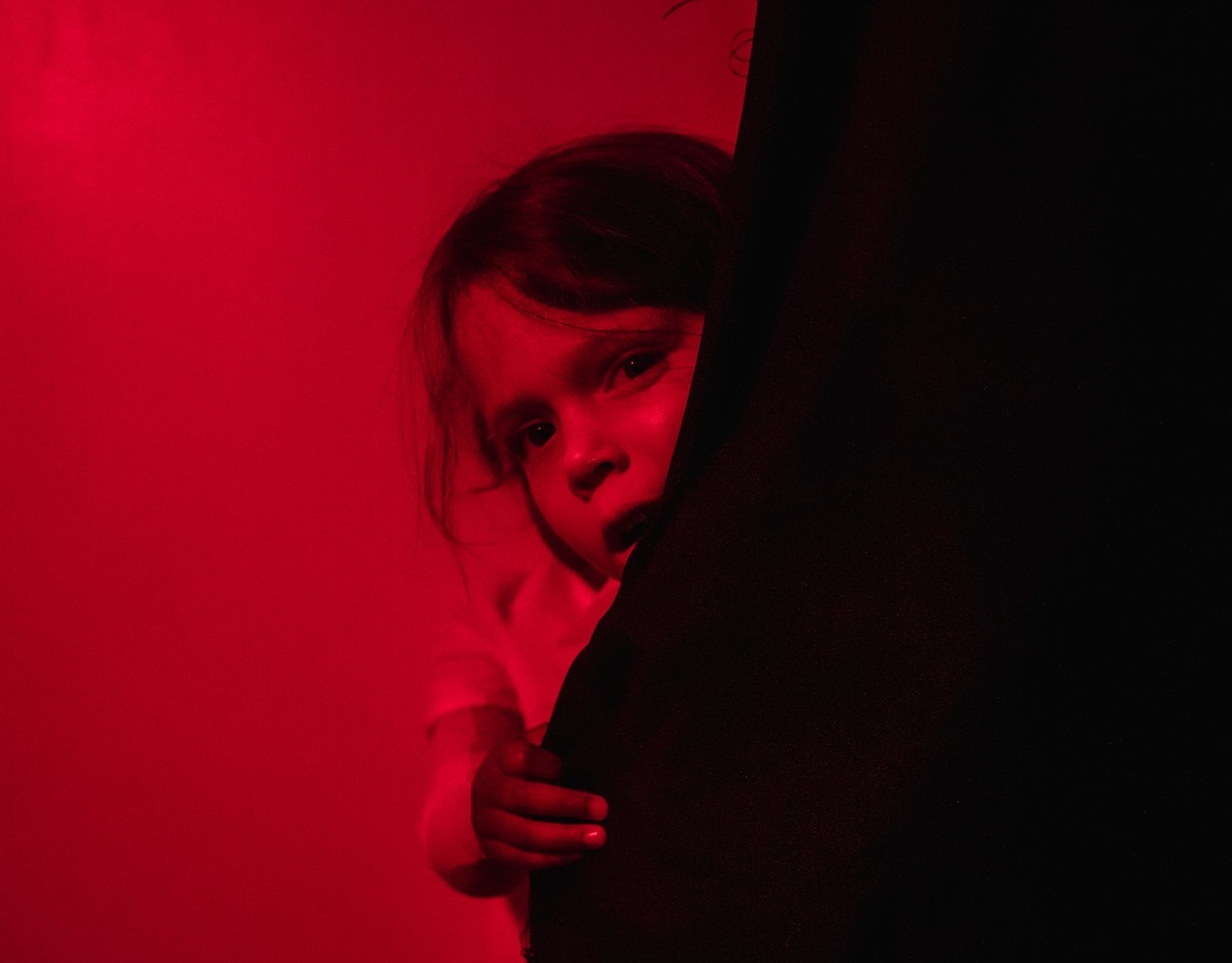Scared young girl is hiding behind wall curtain.