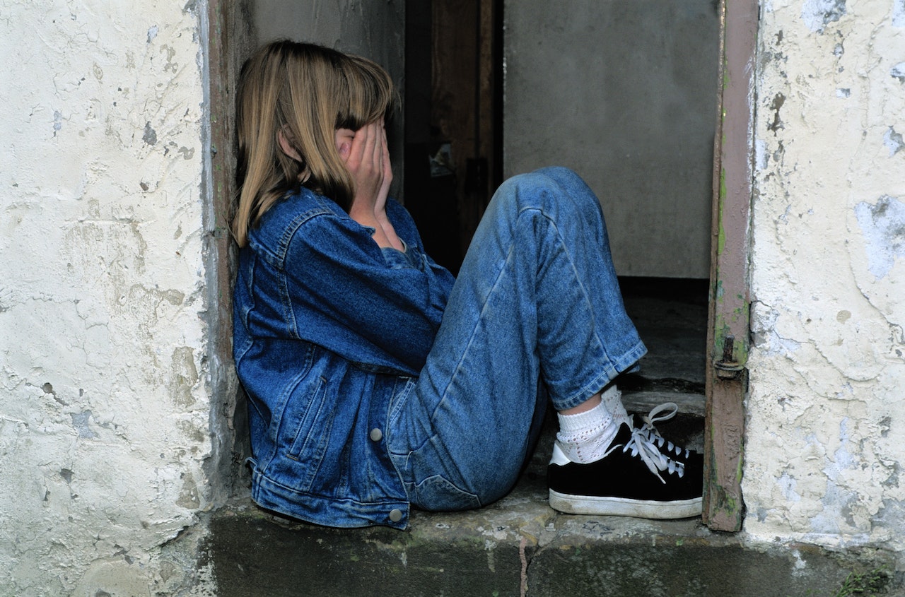 Sad girl wearing blue denim jacket is seating alone on the floor.