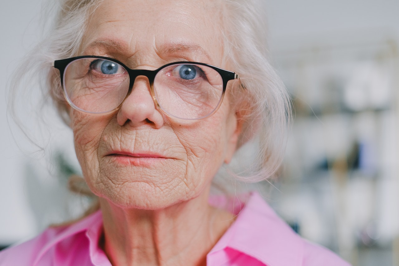 Elder woman wearing pink shirt and glasses is looking at camera.