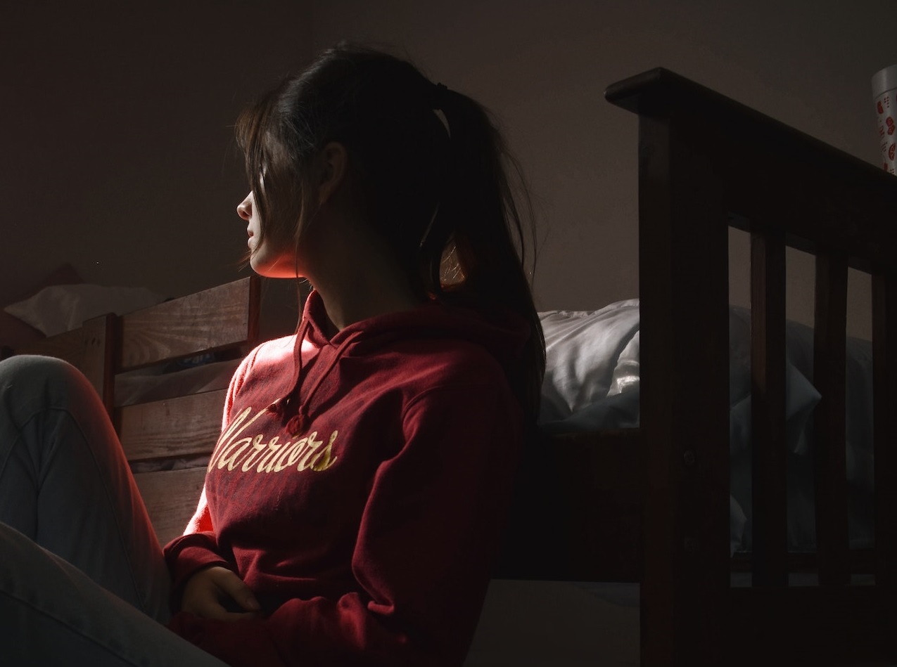 Young girl is seating on the floor in dark room.