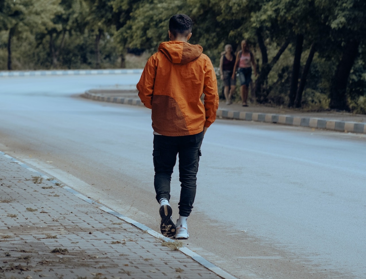 Young man is walking alone on the side of the road.