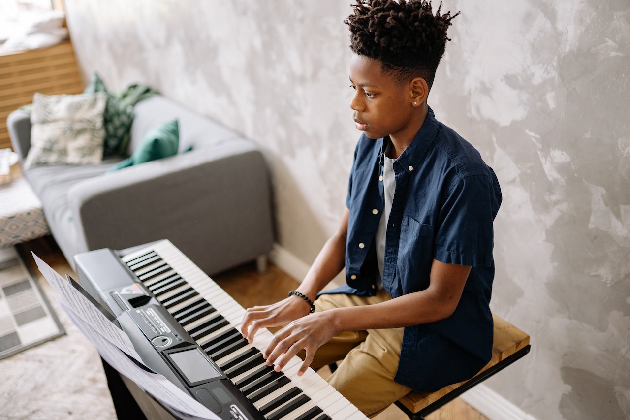 Young black kid is playing on black electric piano in his room.