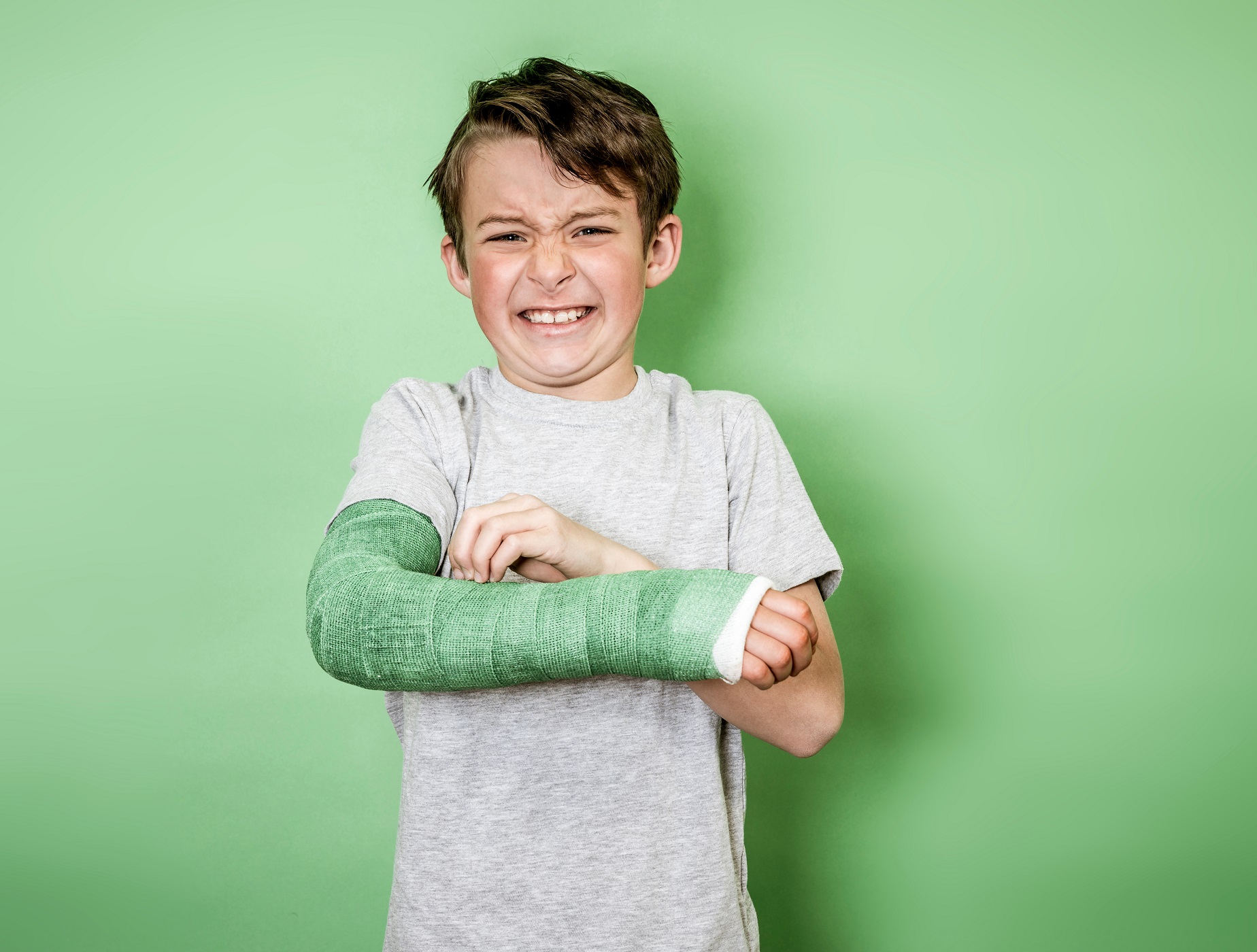 Kid wearing white shirt and cast on his hand is making painful face.