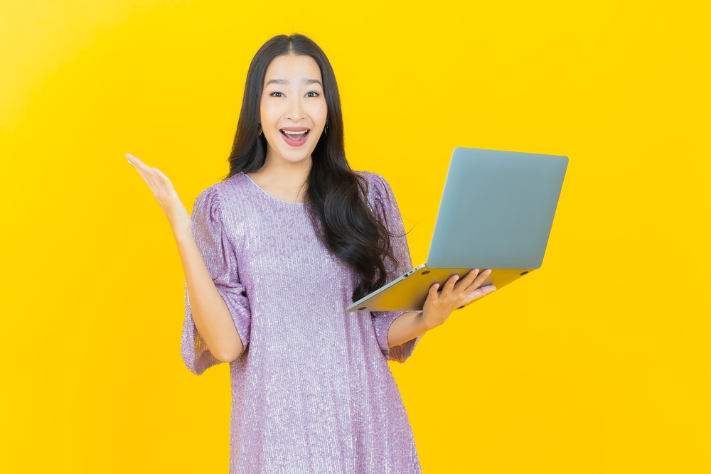 Portrait beautiful young Asian woman smiling  with computer laptop  in pink dress