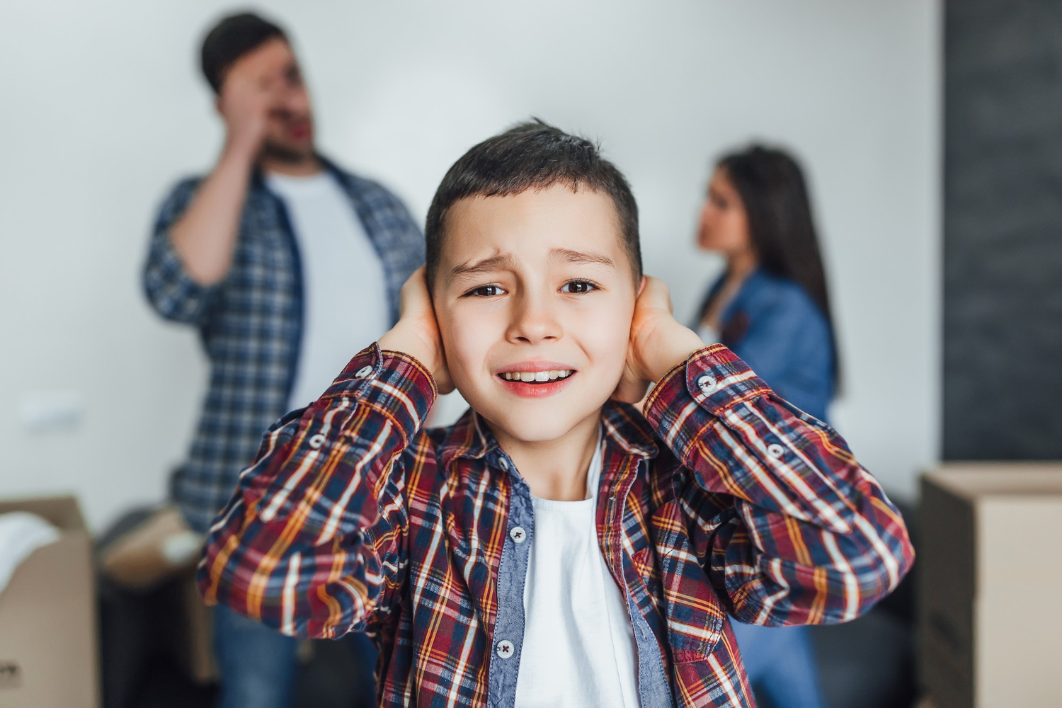 Small kid is crying and covering his ears with his parents standing behind him and yelling.