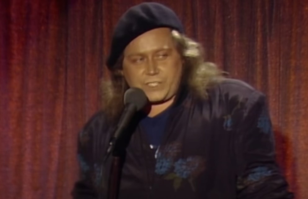Sam Kinison in blue suit and hat giving a monologue