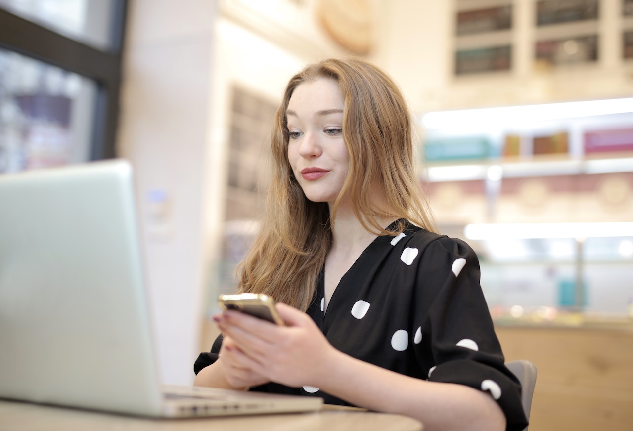 Woman is holding a phone while working on the lap top.
