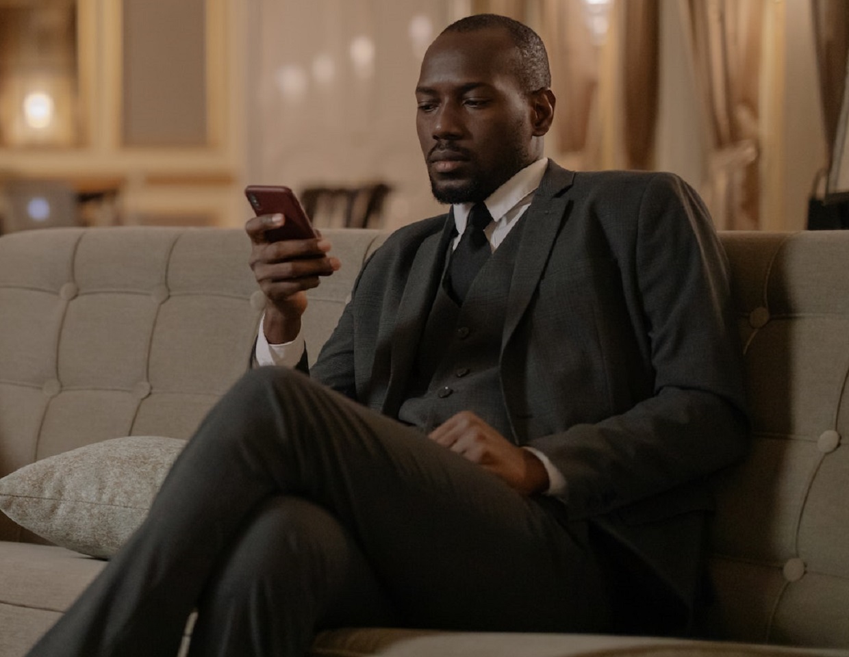 Man wearing a suit is seating on the sofa and texting.