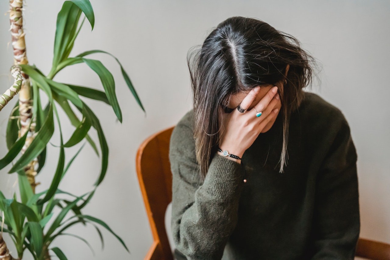 Sad young woman is looking down and holding her head.