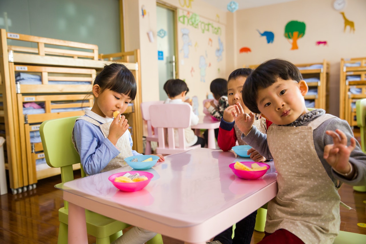 Kids are seating on pink tables in daycare.