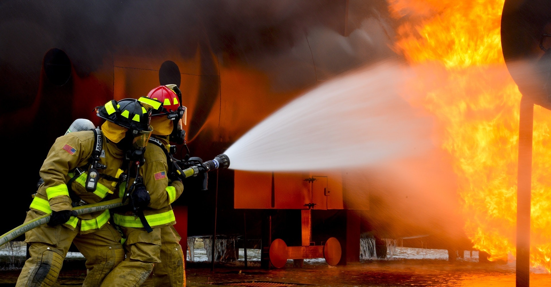 Fireman are trying to put out a fire burning in old barn, holding a fire hose.