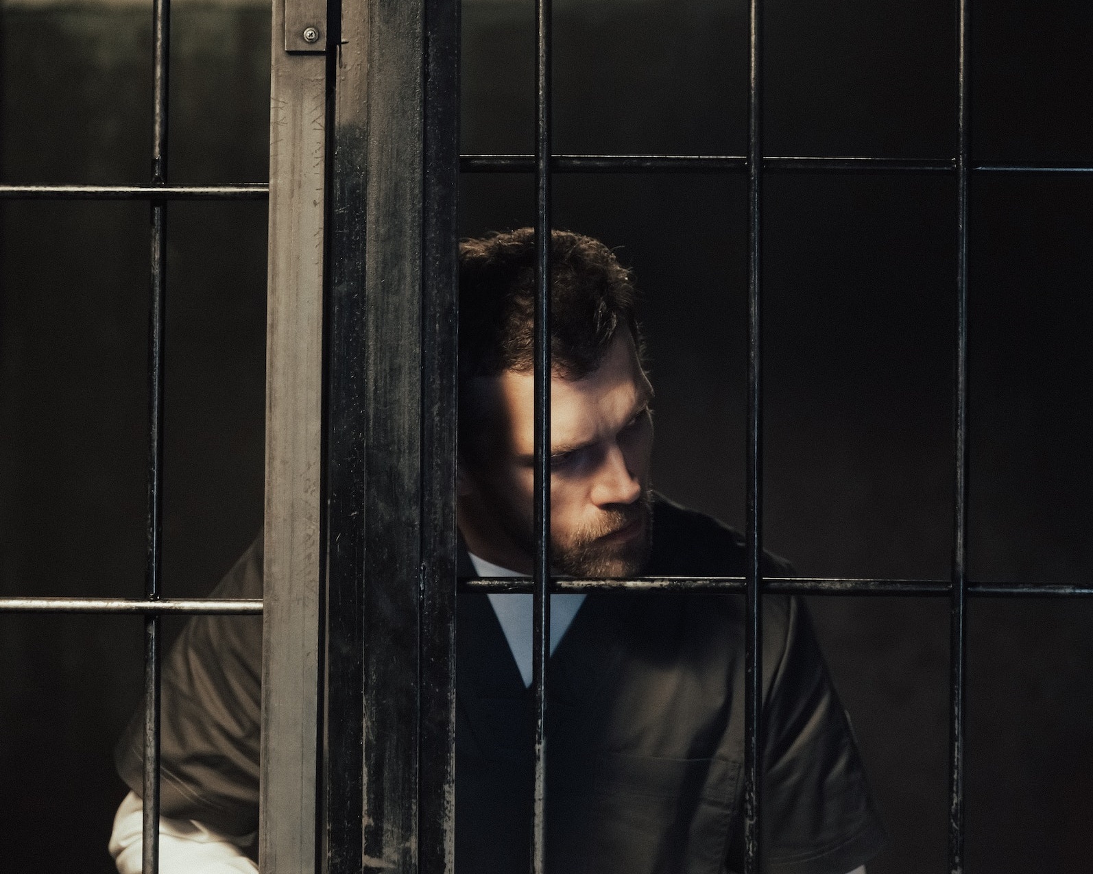 Young man is standing behind bars in jail.