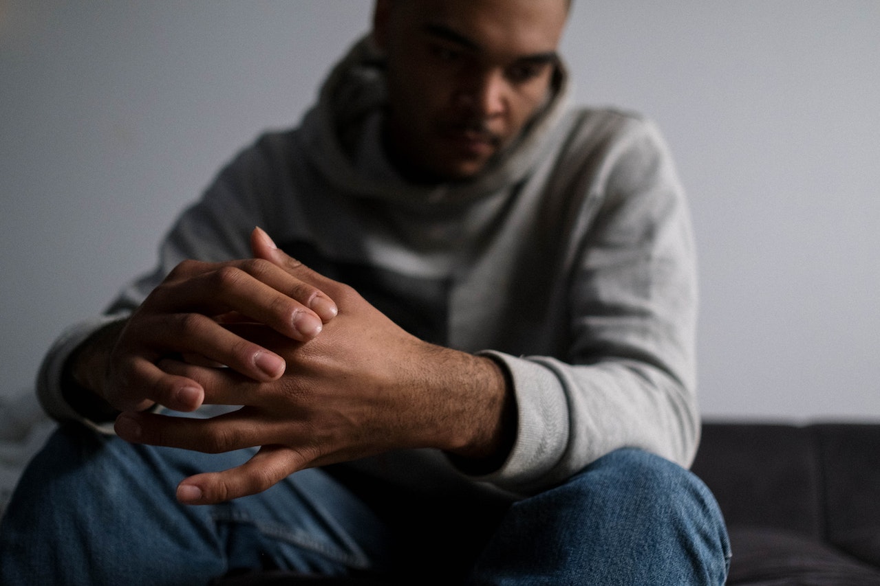 Man wearing grey hoodie is seating on the bed and thinking.