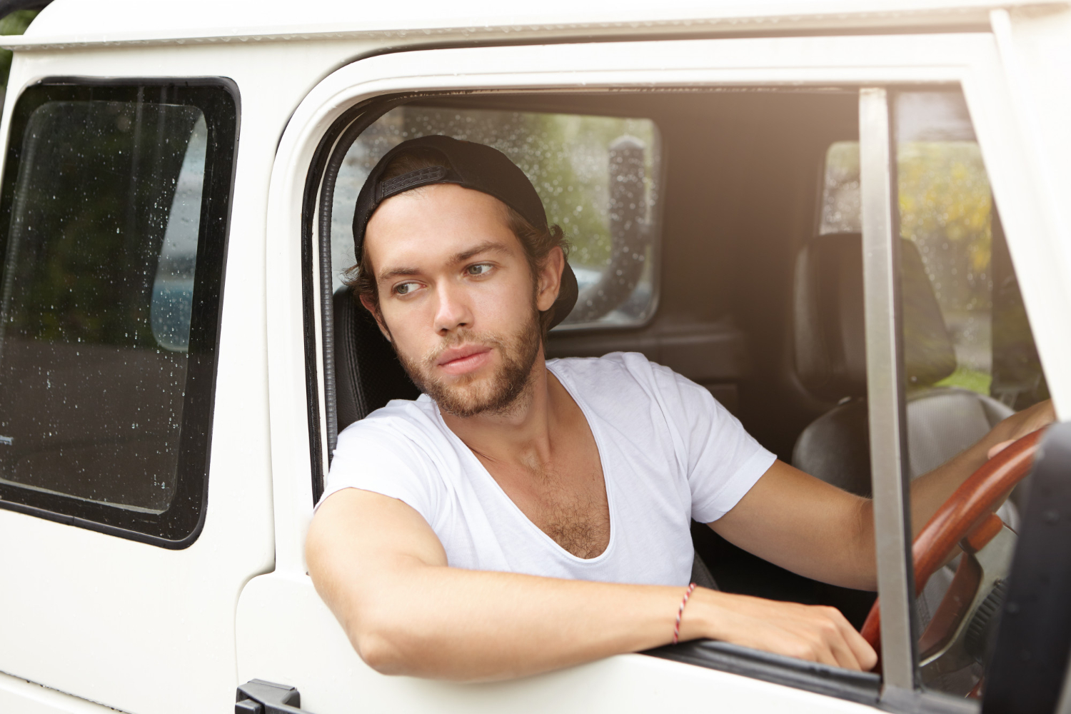 Young man is seating in his old white truck ,looking at side.