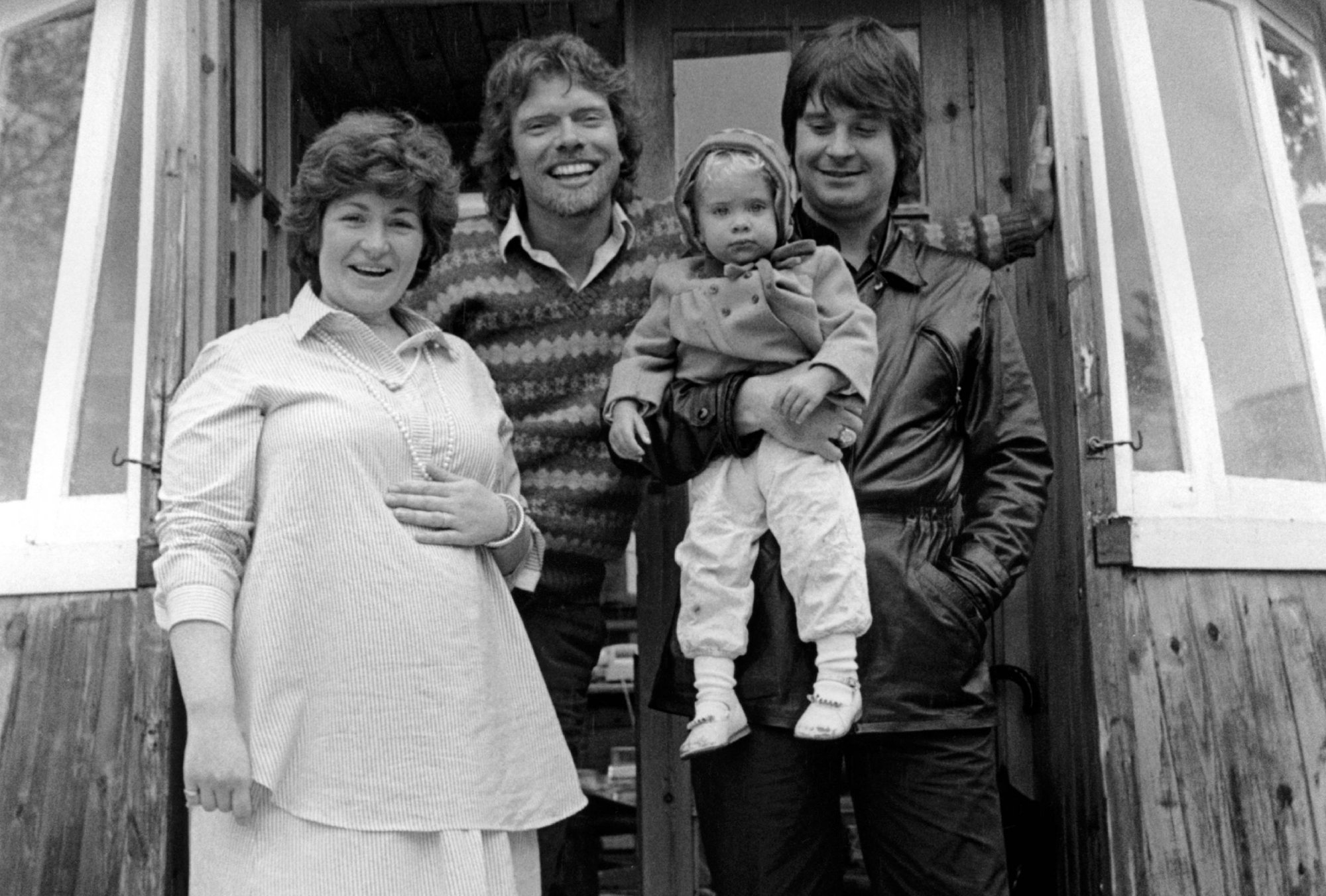 Sharon Osbourne, Richard Branson, Aimee Osbourne (baby), Ozzy Osbourne in front of a wooden cabin