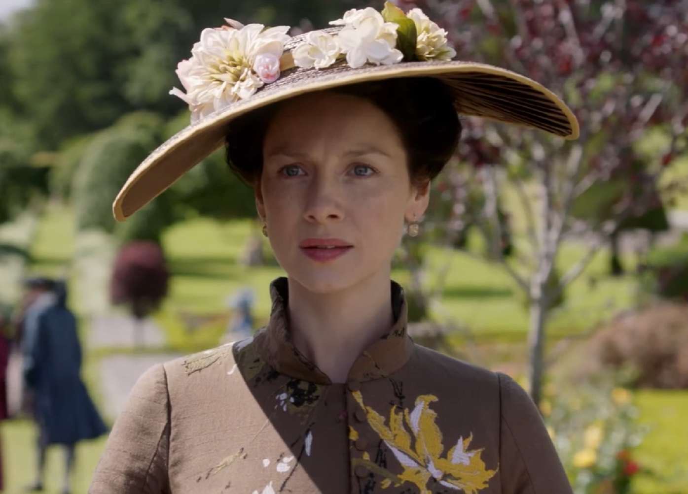 Screenshot: Claire Fraser (Caitríona Balfe) wearing brown dress and brown hat with flowers - from Outlander (Tv Series)