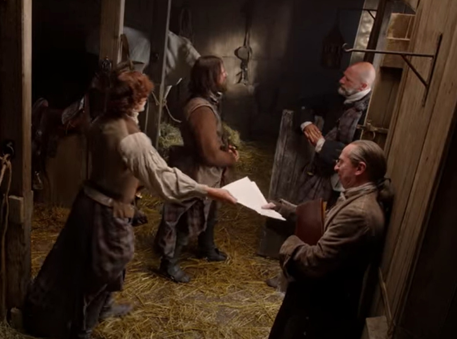 Screenshot: Actors wearing kilts are talking inside a barn - from Outlander (Tv Series)