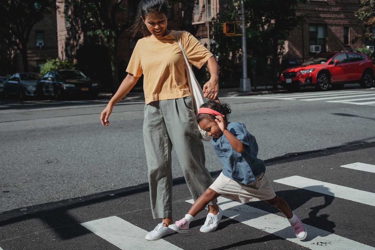 Mother and daughter are crossing the street on crosswalk.