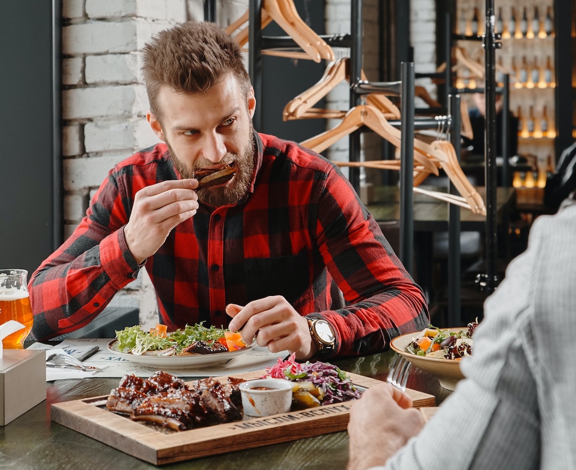 Young bearded man is having a dinner and looking at other man.