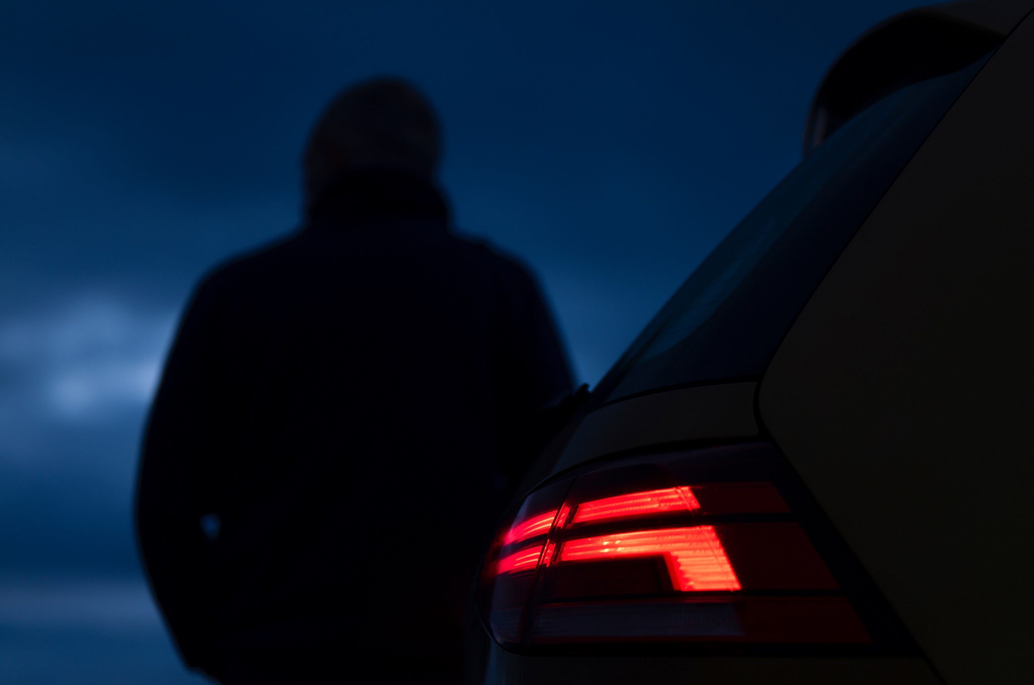 Adult man standing against car looking at side at night time.