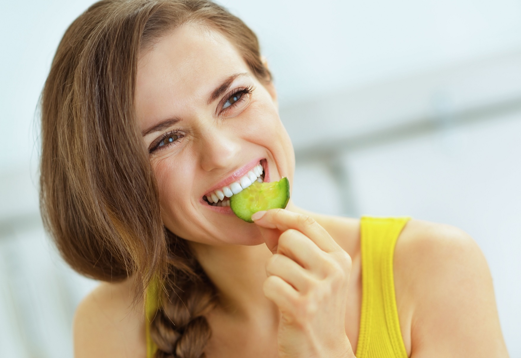 Woman is eating a cucumber and smiling.