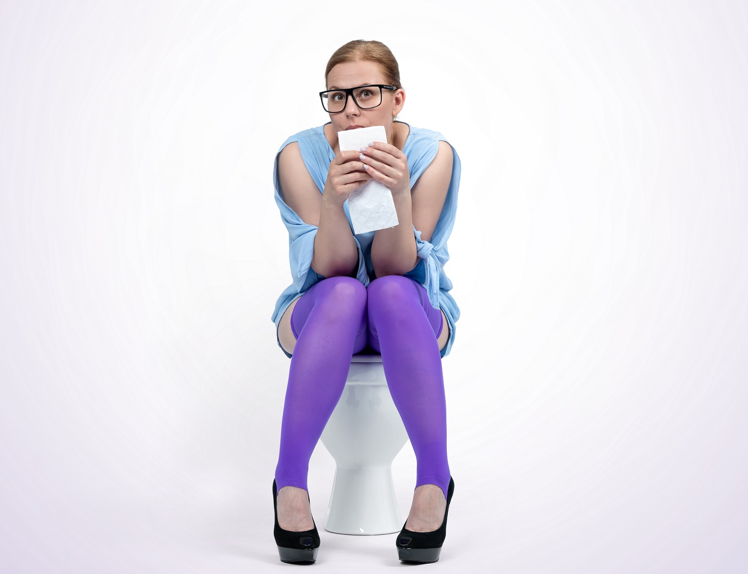 Woman is seating on toilet on grey background.