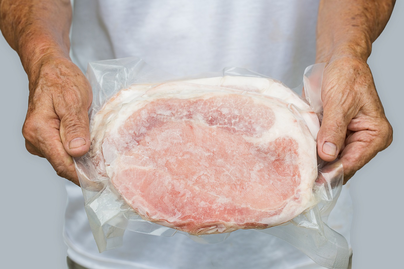 Man wearing white shirt is holding a frozen meat in bag.