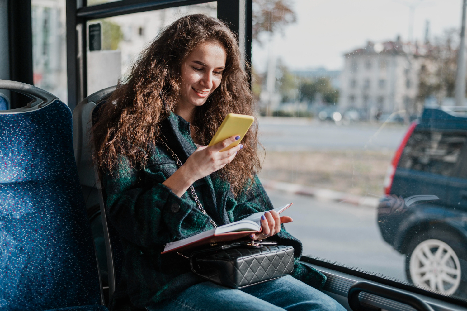 Young woman is seating on the bus and holding a notebook and phone.