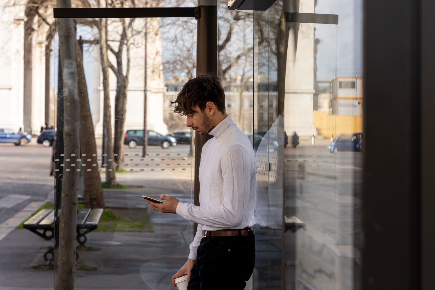 Man is standing on bus stop and texting on phone .