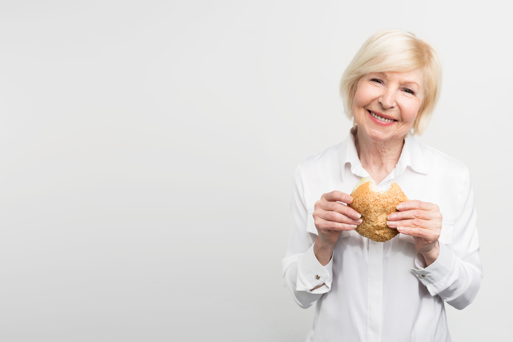Old but satisfied woman in white shirt holding a burger in her hands