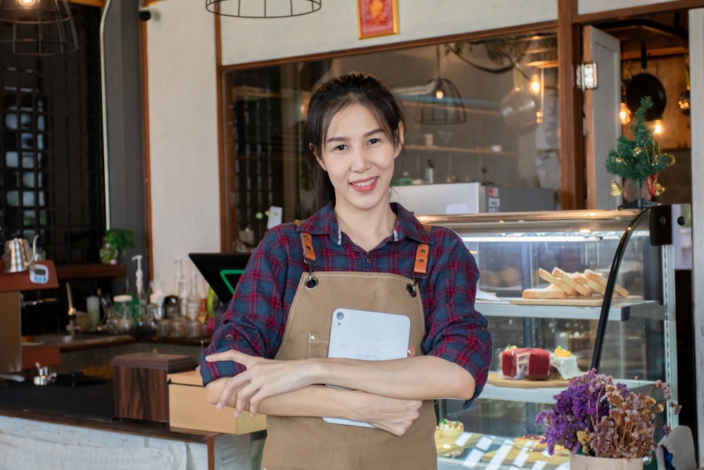 Asian beautiful woman in plaid shirt standing holding tablet in front of the counter