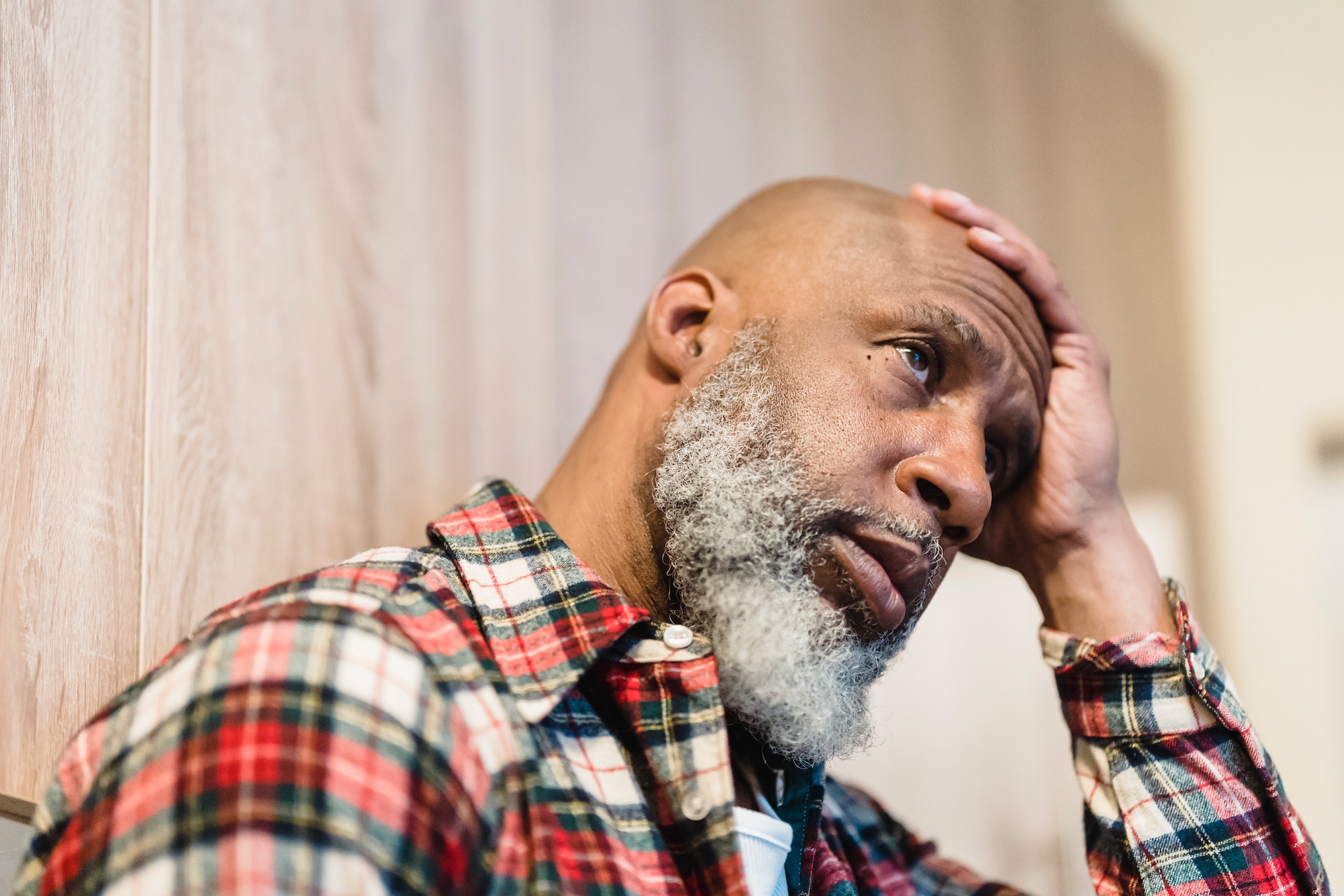 Sad man in plaid shirt sitting at home with his arm on forehead