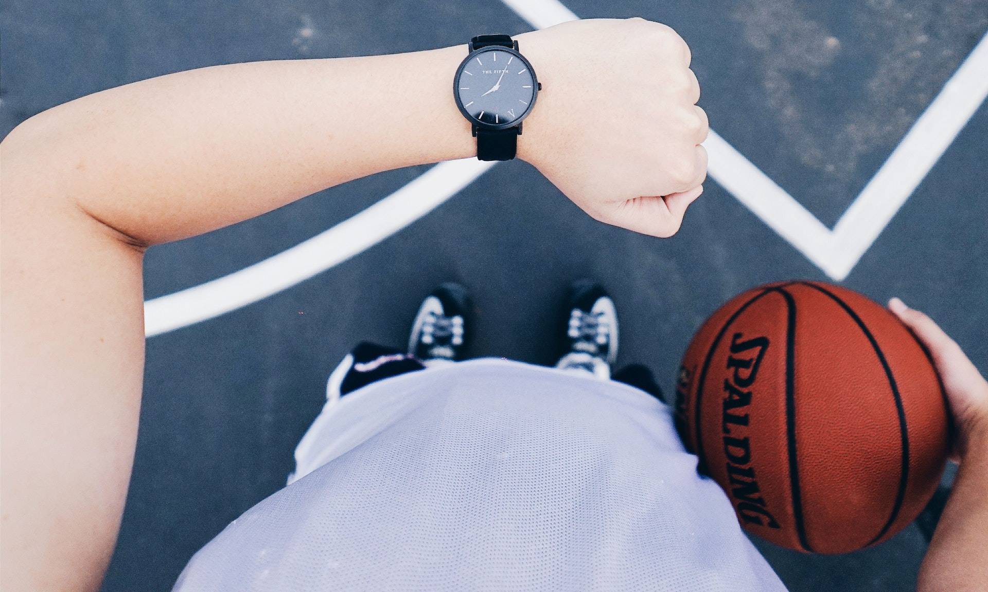 Person in sports wear holding basketball looking at his watch