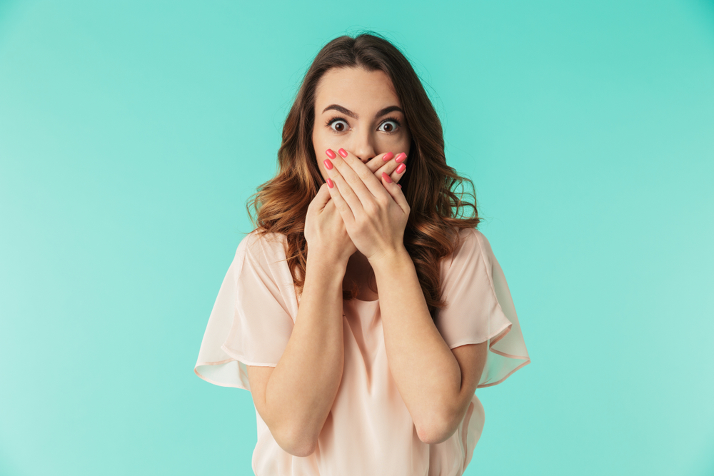 Portrait of a shocked young girl in pink dress looking at camera with mouth covered
