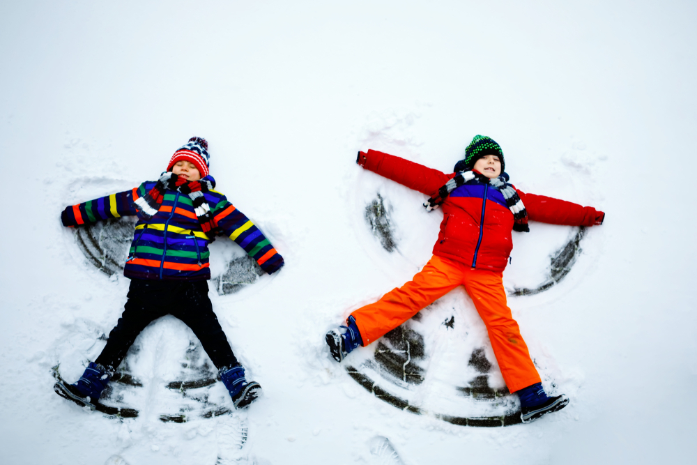 Two little  kid boys in colorful winter clothes making snow angel