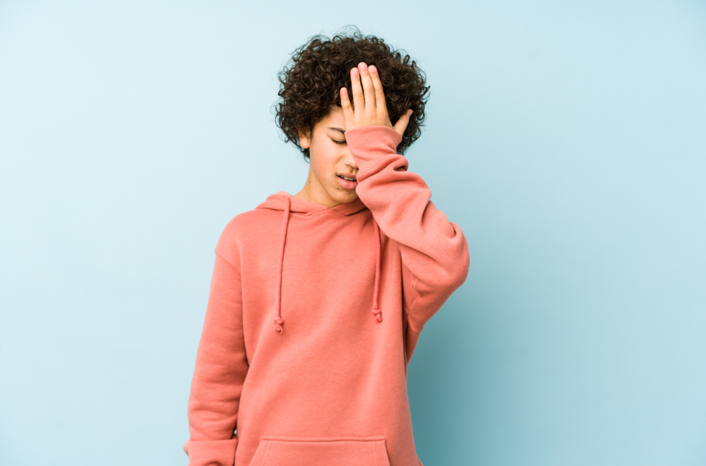 African American little boy slapping his forehead with palm and closing his eyes as if he realized something in orange sweatshirt