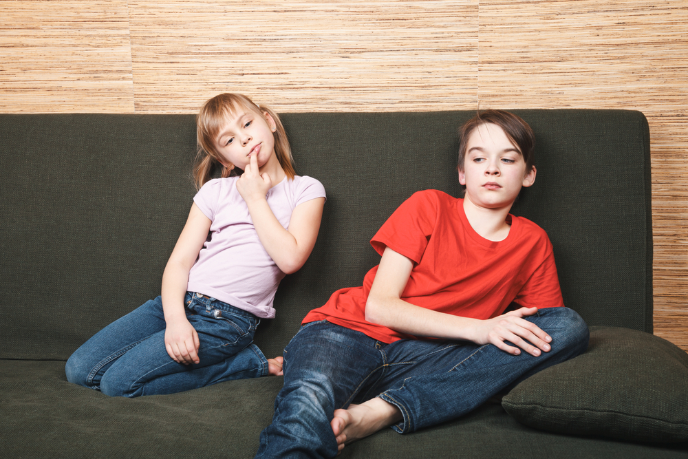 Frustrated siblings sitting on sofa angry at each other in t-shirts and jeans