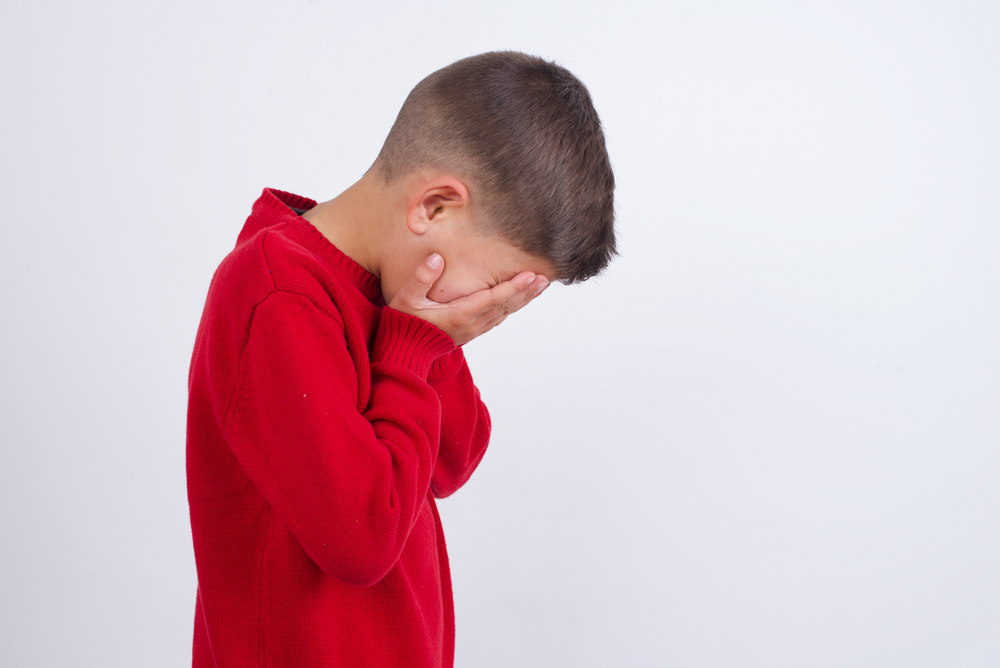 Sad Cute  boy wearing red knitted sweater  covering face with hands and crying