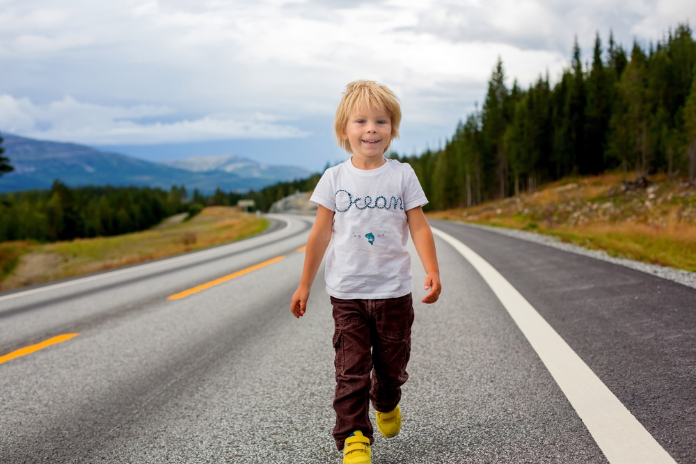 Beautiful blond child in white t-shirt , standing in the middle of the highway