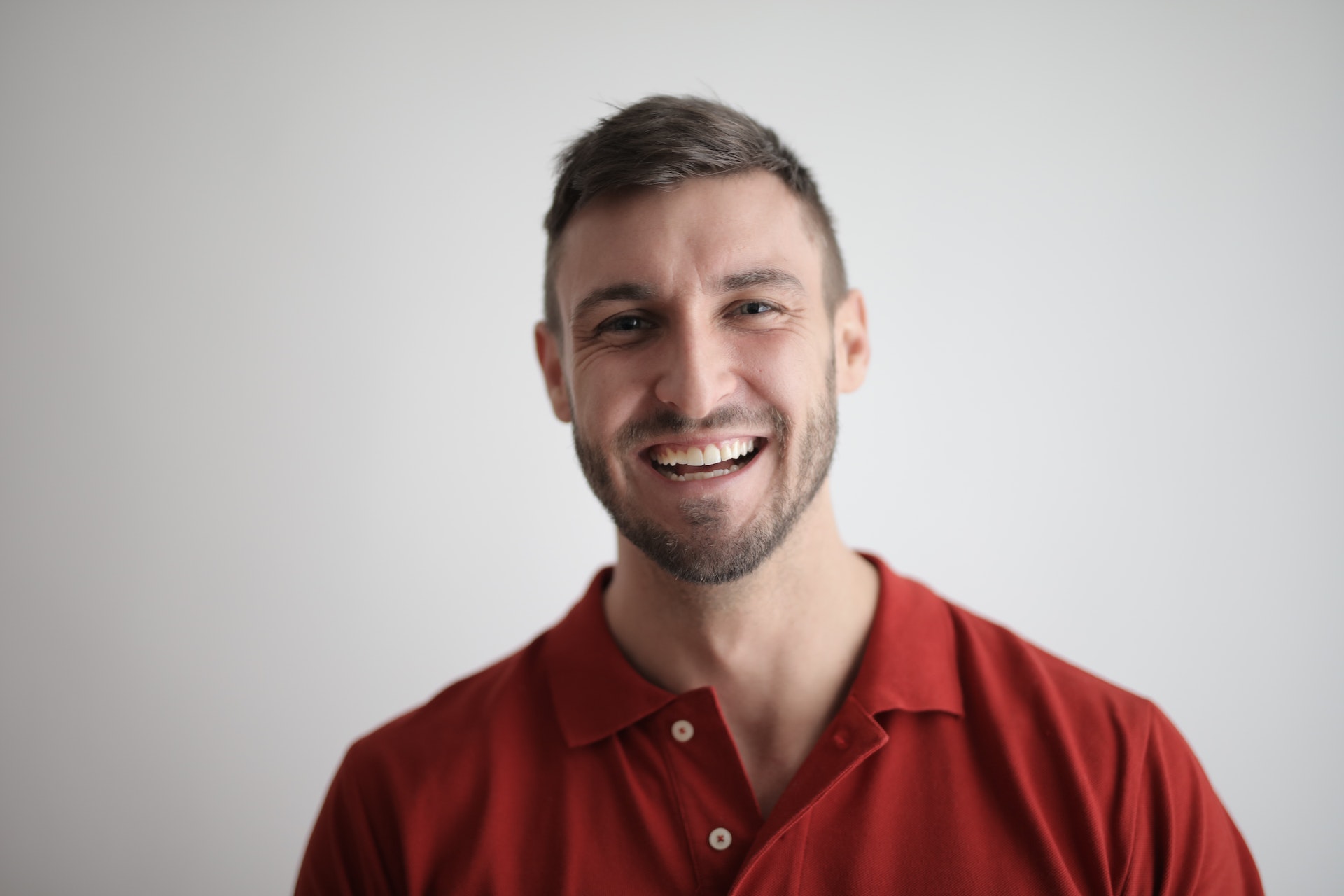 Man in red polo shirt laughing in front of a gray background