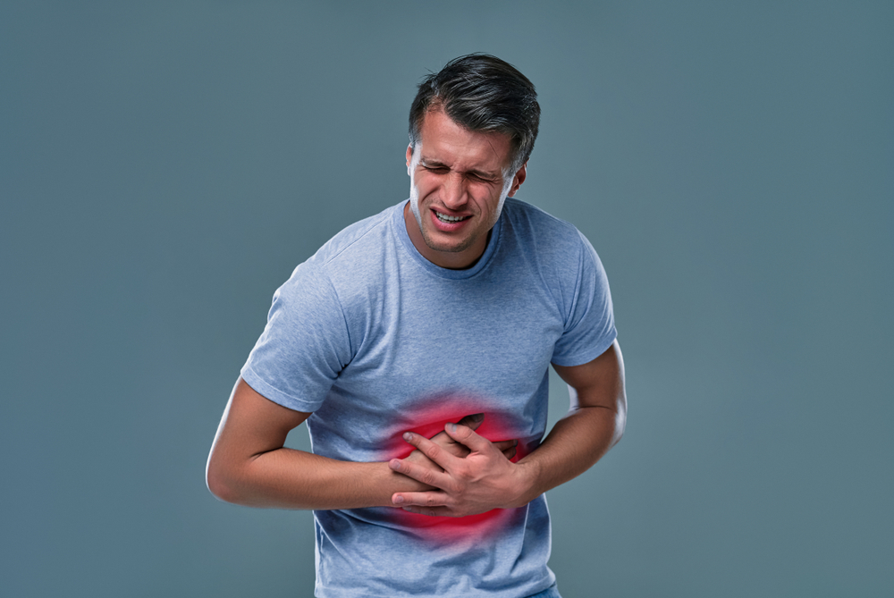 Man in blue t-shirt touching his stomach because of stomach pain