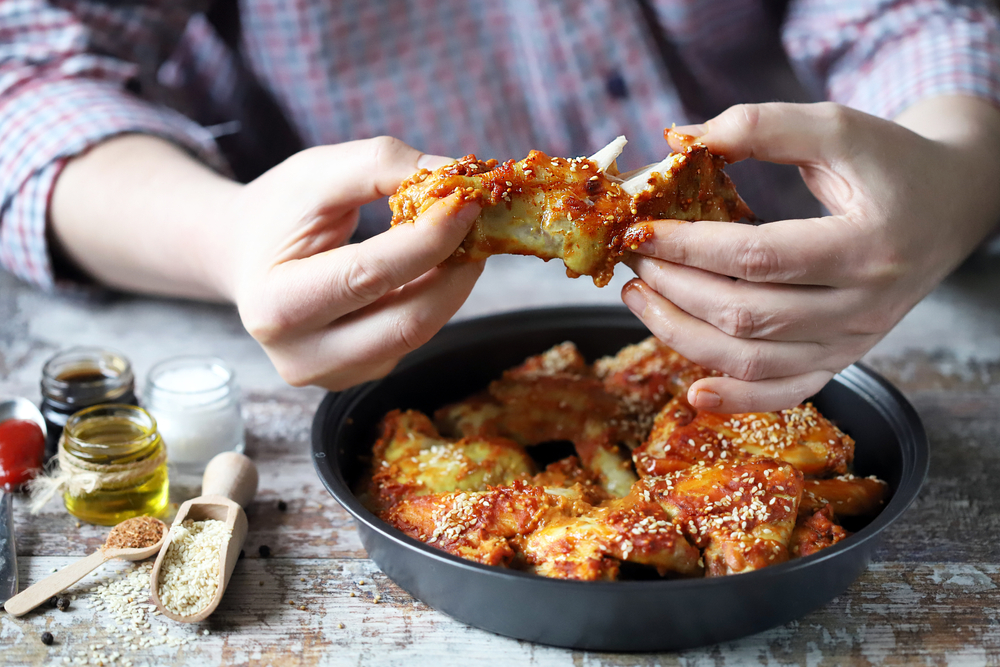 A man in plaid shirt eating chicken wings with his hands