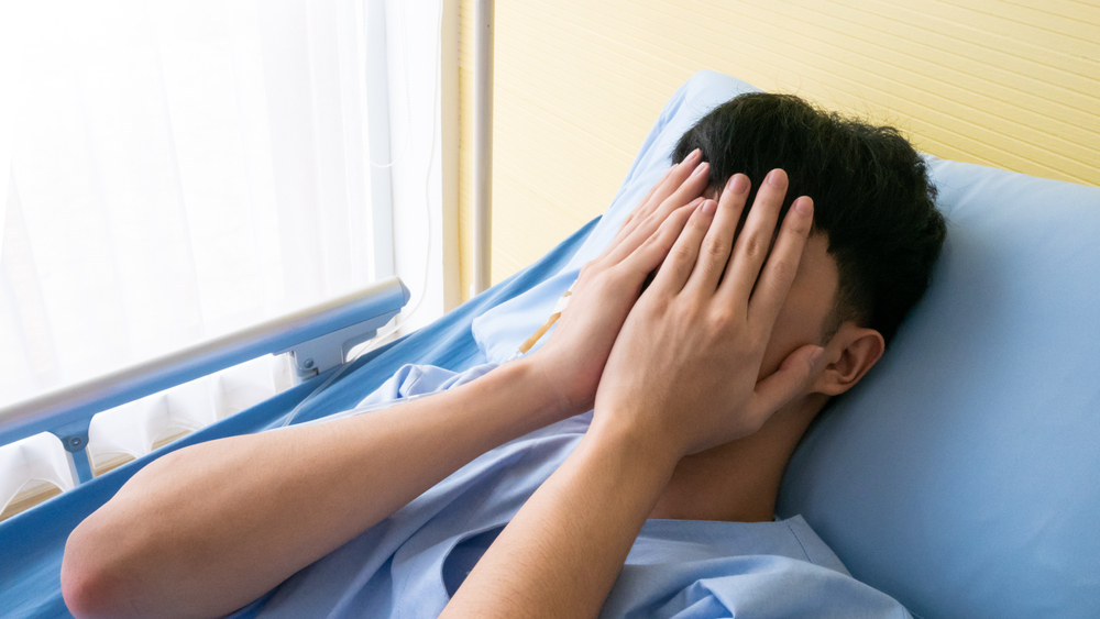 young male covering his face with hands lying in  hospital bed