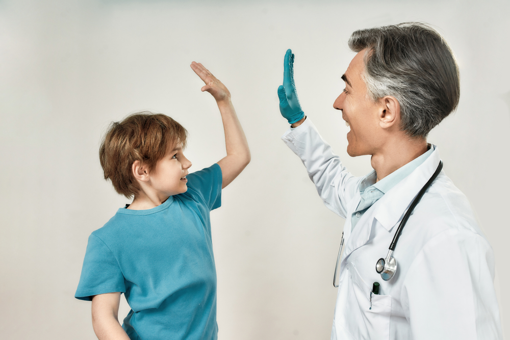 Friendly mature doctor pediatrician giving high five to a happy little boy in blue t-shirt