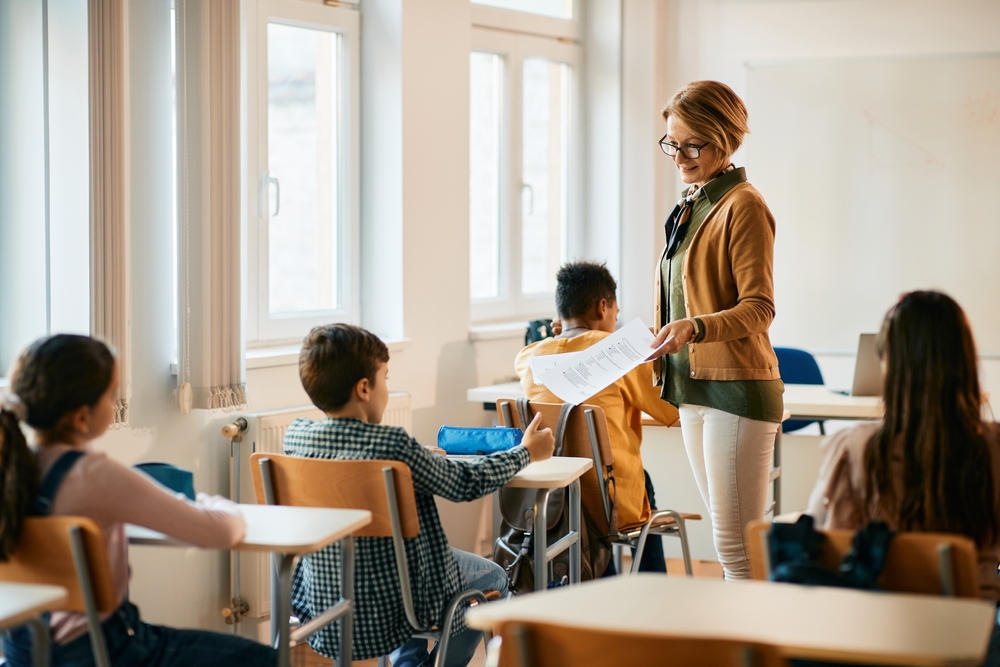 Elementary school teacher  in brown sweater giving test results to her students