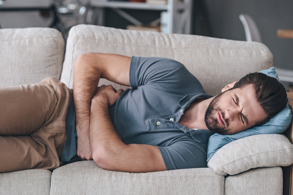 Man in gray t-shirt  suffering form  stomach pains laying on  a couch