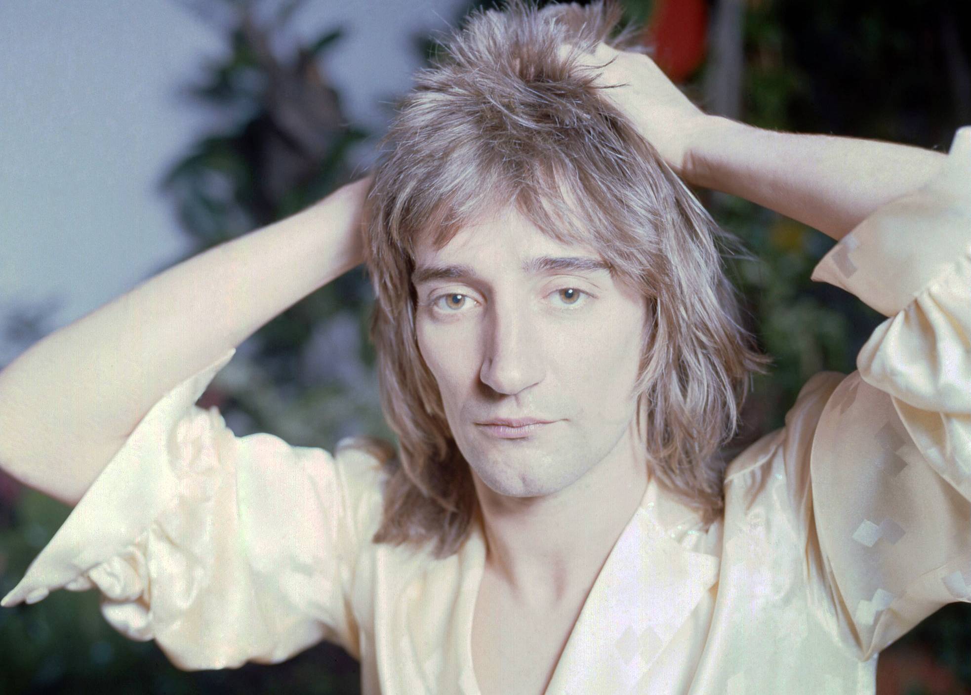 Rod Stewart in white shirt with his hands on his head looking at the camera