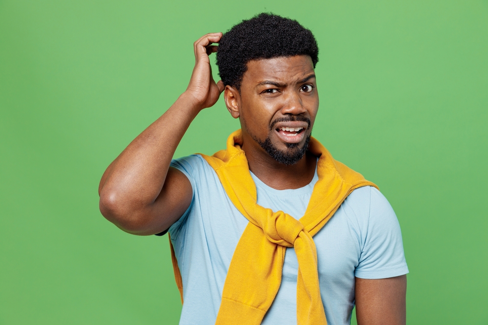 Young sad confused   man of African American ethnicity  scratching his  head
